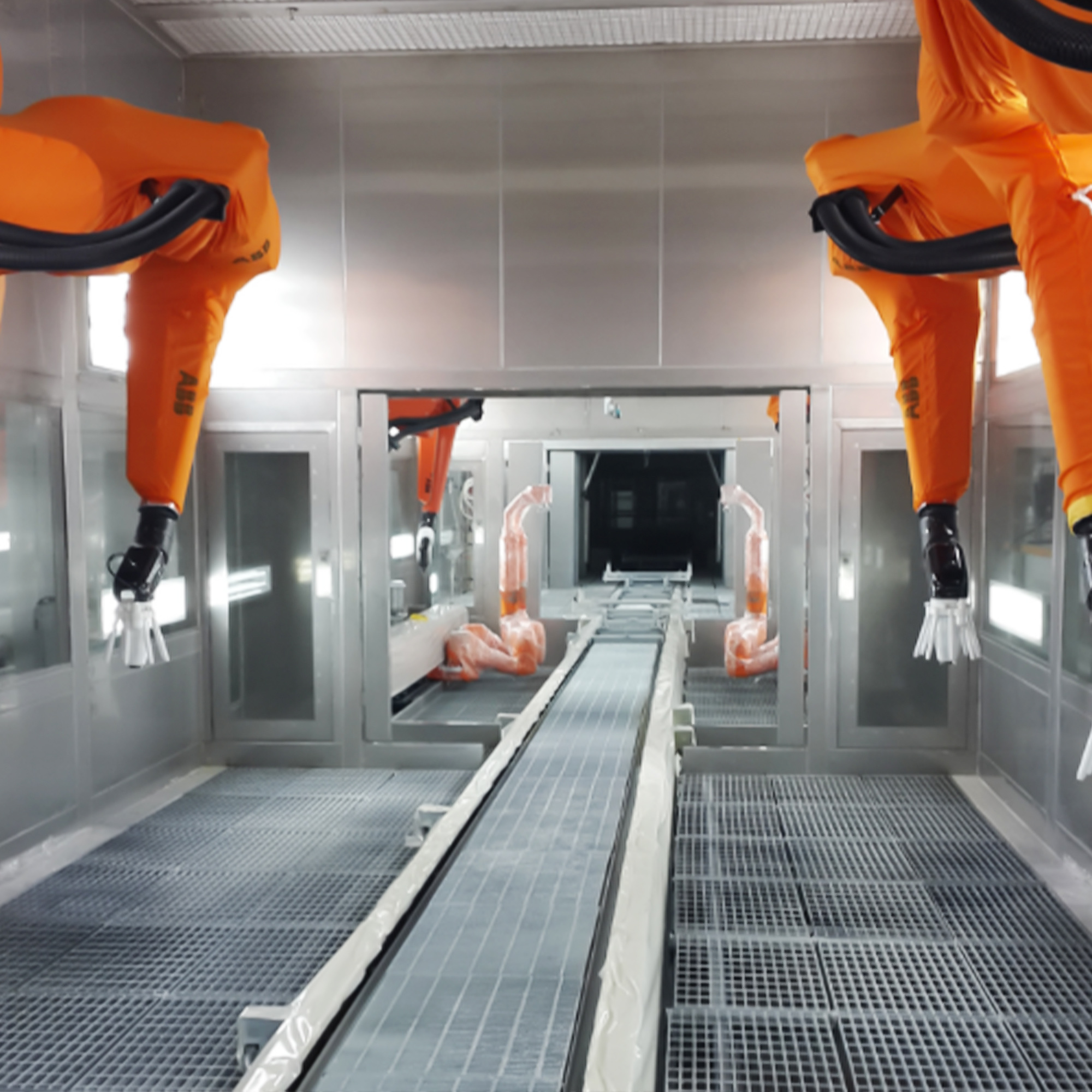 Multiple orange robotic arms with electrostatic spray applicators inside an enclosed booth