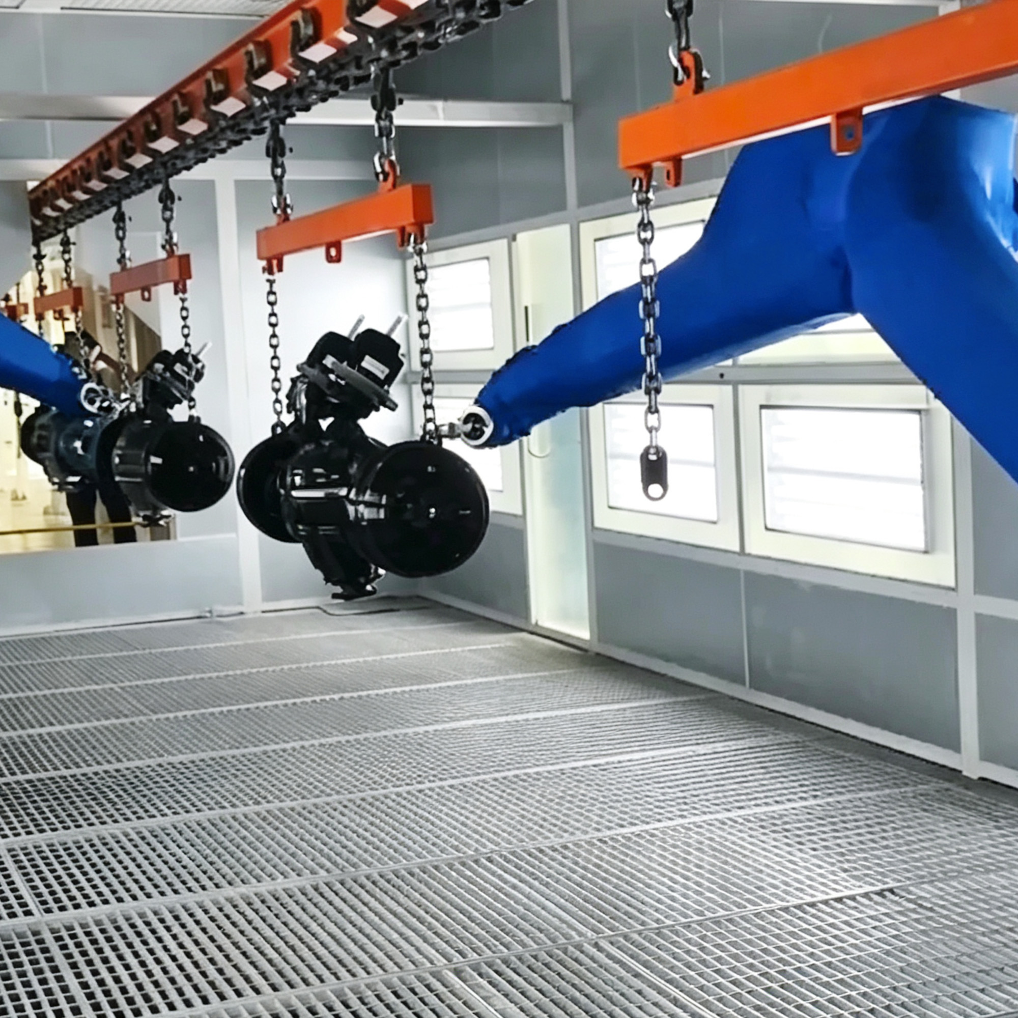 Blue robotic arms painting black component wheels suspended from an overhead conveyor