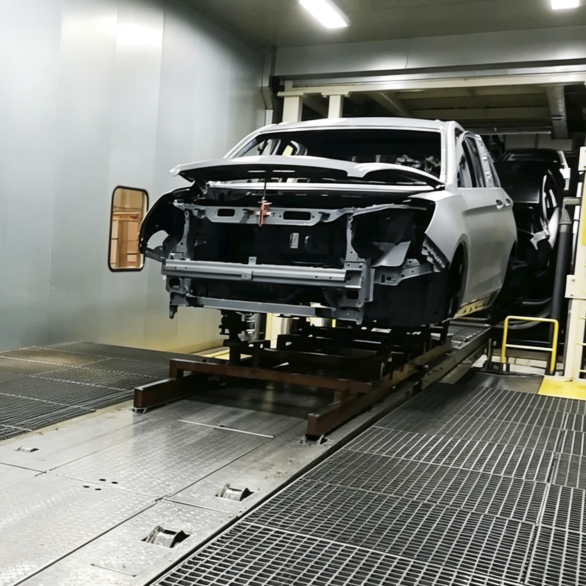 Primed passenger vehicle body shell suspended on a conveyor inside a spray booth